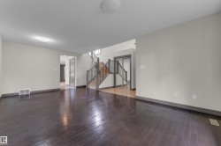 Expansive room featuring dark wood-finish flooring, light-toned walls, and a visible air vent - 