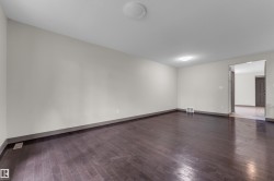 Spacious interior room featuring dark wood-finish flooring, light-toned wall paint, and a neutral baseboard trim - 