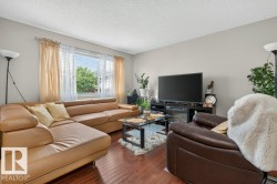 Living area featuring wood-finish flooring, a large window with horizontal blinds, and light-toned wall paint - 