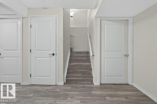 Interior hallway featuring light wood-finish flooring, three paneled doors, and a staircase with a white railing - 692 Secord Boulevard Nw, Edmonton, AB - Indoor Photo Showing Other Room