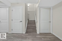Interior hallway featuring light wood-finish flooring, three paneled doors, and a staircase with a white railing - 
