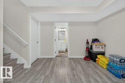 Finished basement area featuring wood-finish flooring, light grey walls, white trim, and a white interior door - 