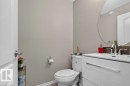 Contemporary powder room featuring a white single-sink vanity with chrome hardware, an oval frameless mirror, and a brown mosaic tile backsplash - 692 Secord Boulevard Nw, Edmonton, AB  - Indoor Photo Showing Bathroom 