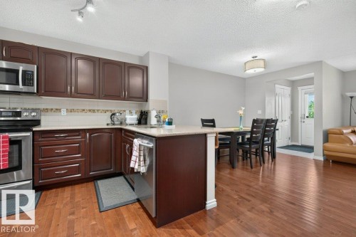 Kitchen with wood-finish flooring, dark wood cabinetry, stainless steel appliances, and light-toned countertops - 692 Secord Boulevard Nw, Edmonton, AB - Indoor Photo Showing Kitchen