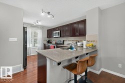 Kitchen featuring dark wood cabinetry, light-toned countertops, tile backsplash, and wood-finish flooring - 