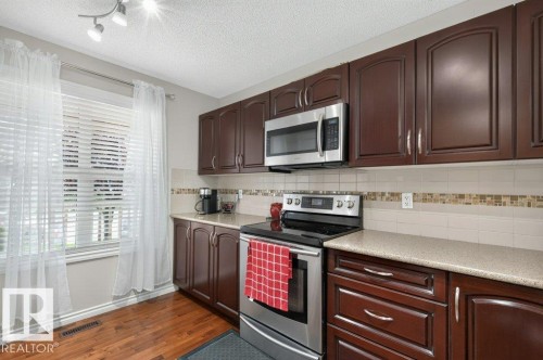 Kitchen featuring dark wood-finish cabinetry with silver hardware, light-toned countertops, and a tile backsplash with decorative mosaic accent - 692 Secord Boulevard Nw, Edmonton, AB - Indoor Photo Showing Kitchen