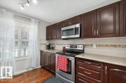 Kitchen featuring dark wood-finish cabinetry with silver hardware, light-toned countertops, and a tile backsplash with decorative mosaic accent - 