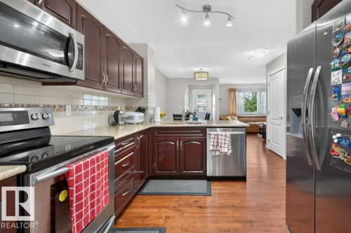 Well-appointed kitchen featuring wood-finish flooring, stainless steel appliances, dark wood cabinetry, light-toned countertops, and a tiled backsplash - 692 Secord Boulevard Nw, Edmonton, AB - Indoor Photo Showing Kitchen