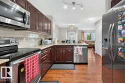 Well-appointed kitchen featuring wood-finish flooring, stainless steel appliances, dark wood cabinetry, light-toned countertops, and a tiled backsplash - 