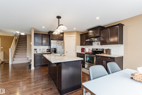 Open concept kitchen featuring dark wood cabinetry, stainless steel appliances, a center island with a granite-style countertop, and hardwood flooring - 2605 Anderson Crescent Sw, Edmonton, AB - Indoor Photo Showing Kitchen With Double Sink