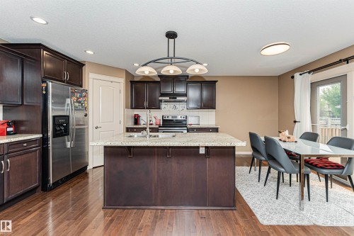 Open-concept kitchen and dining area featuring rich wood-finish flooring, dark wood cabinetry, a central island with a light-toned countertop, and stainless steel appliances - 2605 Anderson Crescent Sw, Edmonton, AB - Indoor