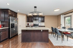 Open-concept kitchen and dining area featuring rich wood-finish flooring, dark wood cabinetry, a central island with a light-toned countertop, and stainless steel appliances - 