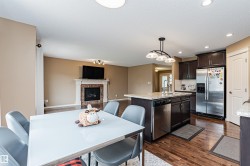 Open-concept living space featuring wood-finish flooring, a kitchen island with integrated dishwasher, stainless steel appliances, and a fireplace with a stone surround - 