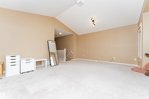 Spacious room featuring vaulted ceilings, light-toned carpeting, a window with white trim, and neutral wall tones - 2605 Anderson Crescent Sw, Edmonton, AB - Indoor Photo Showing Other Room