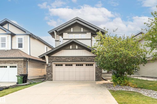 Contemporary two-story exterior featuring a double-car garage with paneling, stone facade accents, light-toned siding, dark trim, and multiple windows - 2605 Anderson Crescent Sw, Edmonton, AB - Outdoor