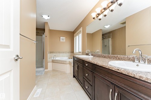 Spacious bathroom featuring a double vanity with dark wood cabinetry and a speckled countertop, a large mirror, an integrated corner bathtub with tiled surround, and a glass-enclosed shower - 2605 Anderson Crescent Sw, Edmonton, AB - Indoor Photo Showing Bathroom