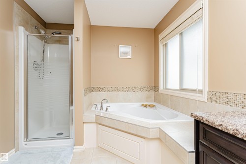 Bathroom featuring a corner soaking tub with tiled surround, a separate glass-enclosed shower, a window with horizontal blinds, and a vanity with a stone-finish countertop - 2605 Anderson Crescent Sw, Edmonton, AB - Indoor Photo Showing Bathroom