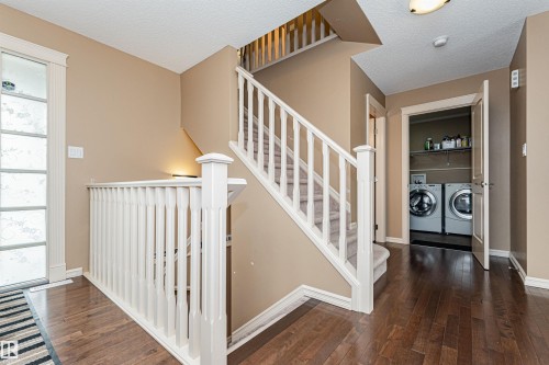 Hardwood flooring throughout the hallway, leading to a carpeted staircase with white balusters - 2605 Anderson Crescent Sw, Edmonton, AB - Indoor Photo Showing Other Room