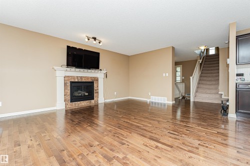 Living area featuring wood-finish flooring, a fireplace with a stone surround and white mantel, and neutral wall tones - 2605 Anderson Crescent Sw, Edmonton, AB - Indoor Photo Showing Living Room With Fireplace