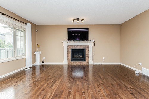 Spacious living area featuring rich wood-finish flooring, a prominent fireplace with a stone surround and white mantel, and a large multi-pane window - 2605 Anderson Crescent Sw, Edmonton, AB - Indoor Photo Showing Living Room With Fireplace