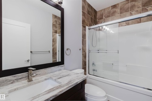 Bathroom featuring a combination tub and shower with a sliding glass enclosure, brown tiled shower surround, dark wood-finish vanity with an integrated sink, brushed nickel faucet, and a framed mirror - 10626 81 Avenue Nw, Edmonton, AB - Indoor Photo Showing Bathroom