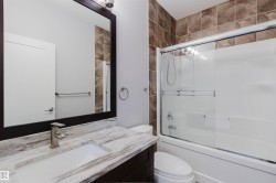 Bathroom featuring a combination tub and shower with a sliding glass enclosure, brown tiled shower surround, dark wood-finish vanity with an integrated sink, brushed nickel faucet, and a framed mirror - 