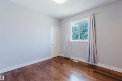 Spacious room featuring rich wood-finish flooring, light gray walls, white baseboards, and a white window frame - 