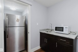 Compact kitchenette featuring dark wood-finish cabinetry, a stone countertop, and an undermount sink with a gooseneck faucet - 