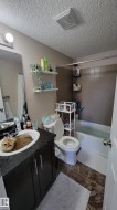 Bathroom featuring a dark wood-finish vanity with a black countertop, a white ceramic sink, and a combination shower-tub with dark tile surround - 