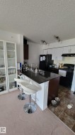 Kitchen featuring white upper cabinetry, dark lower cabinetry, and a dark countertop island with an integrated sink - 