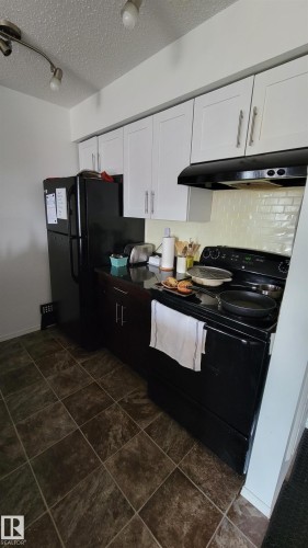 Kitchen featuring white upper cabinetry, dark lower cabinetry, and black appliances - #415 12045 22 Av Sw, Edmonton, AB - Indoor Photo Showing Kitchen