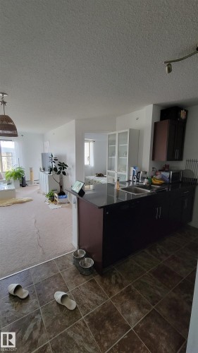 Kitchen area featuring dark cabinetry, a black countertop, and a double-basin stainless steel sink - #415 12045 22 Av Sw, Edmonton, AB - Indoor