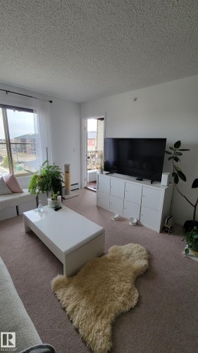 Living area featuring neutral-toned carpet flooring and white painted walls - #415 12045 22 Av Sw, Edmonton, AB - Indoor Photo Showing Living Room
