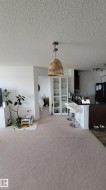 Open-concept living space featuring a woven pendant light fixture, light-toned carpeting, and a kitchen island with built-in seating - 