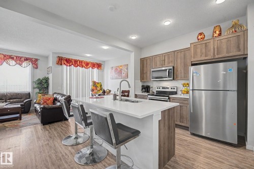 Open-concept kitchen featuring an island with a white countertop, wood-finish flooring, and recessed lighting - 22419 80 Avenue Nw, Edmonton, AB - Indoor Photo Showing Kitchen With Double Sink