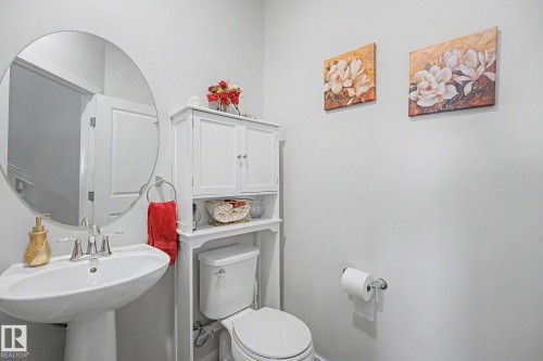 Pedestal sink with chrome faucet, circular wall mirror, and white wall cabinet with built-in shelving - 22419 80 Avenue Nw, Edmonton, AB - Indoor Photo Showing Bathroom