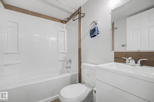 Bright bathroom featuring a white tub/shower combination with integrated shelving, a white vanity with an integrated sink, chrome fixtures, and a wood-finish accent wall - 22419 80 Avenue Nw, Edmonton, AB - Indoor Photo Showing Bathroom