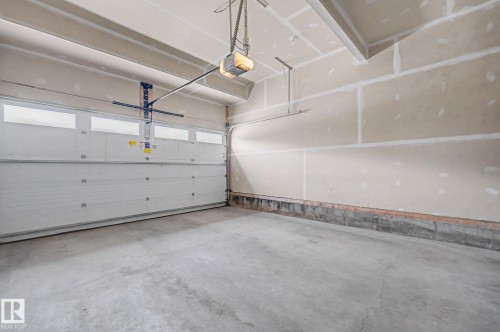 Two-car garage featuring a sectional overhead door with window panels, automatic opener, concrete flooring, and unfinished drywall walls - 22419 80 Avenue Nw, Edmonton, AB - Indoor Photo Showing Garage