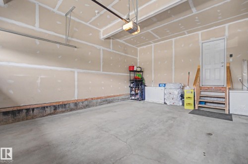Concrete floor garage featuring an automatic garage door opener, a side entry door with wood stairs, and neutral-toned unfinished drywall - 22419 80 Avenue Nw, Edmonton, AB - Indoor Photo Showing Garage