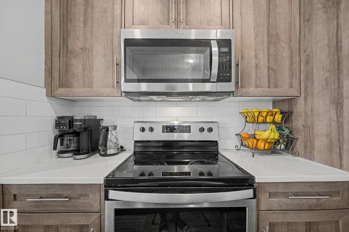 Stainless steel oven and microwave, white subway tile backsplash, light wood-finish cabinetry, and white countertops - 22419 80 Avenue Nw, Edmonton, AB - Indoor Photo Showing Kitchen