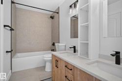 Modern bathroom featuring a dual vanity with light wood-finish cabinetry, integrated sinks, and matte black fixtures - 