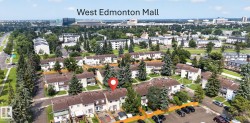 Aerial view of a residential community featuring townhomes with brown roofs and light-colored siding, surrounded by mature evergreen trees - 