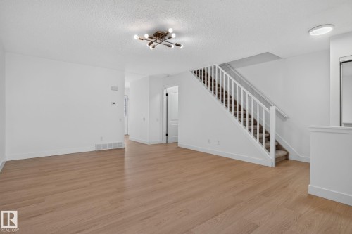 Open-concept living area featuring wood-finish flooring, a modern sputnik light fixture, and a staircase with white railings and carpeted treads - 8059 178 Street Nw, Edmonton, AB - Indoor Photo Showing Other Room