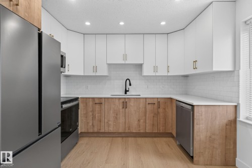 Contemporary kitchen featuring a stainless steel refrigerator, white subway tile backsplash, recessed lighting, wood-finish flooring, and two-tone cabinetry with gold-finish hardware - 8059 178 Street Nw, Edmonton, AB - Indoor Photo Showing Kitchen With Upgraded Kitchen