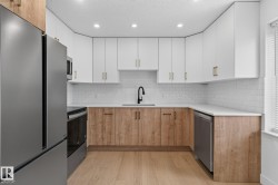 Contemporary kitchen featuring a stainless steel refrigerator, white subway tile backsplash, recessed lighting, wood-finish flooring, and two-tone cabinetry with gold-finish hardware - 