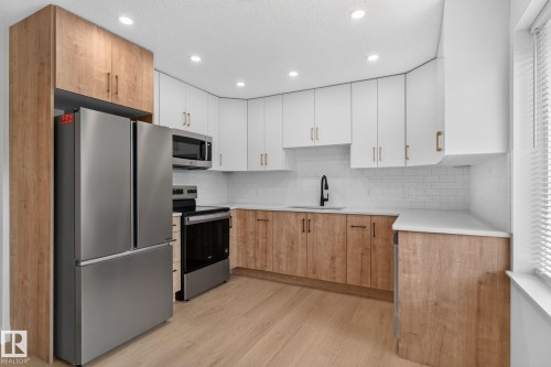 Modern kitchen featuring a stainless steel French door refrigerator, white subway tile backsplash, and two-tone cabinetry with wood-finish base cabinets and white upper cabinets - 8059 178 Street Nw, Edmonton, AB - Indoor Photo Showing Kitchen With Stainless Steel Kitchen With Upgraded Kitchen