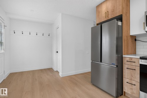 Modern kitchen area featuring wood-finish flooring, white walls, and a stainless steel French-door refrigerator - 8059 178 Street Nw, Edmonton, AB - Indoor Photo Showing Kitchen