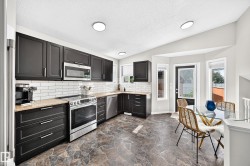 Modern kitchen featuring black cabinetry, light-toned countertops, and a white subway tile backsplash - 