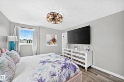 Spacious room featuring light gray walls, wood-finish flooring, a window with exterior views, and a contemporary ceiling light fixture - 