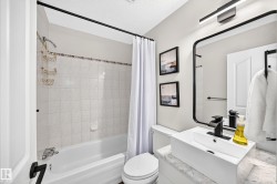 Bathroom featuring a white bathtub, ceramic wall tiling, white vanity with stone-finish countertop, vessel sink, and matte black fixtures - 